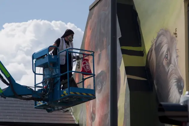 An artist painting portraits from a blue elevated work platform
